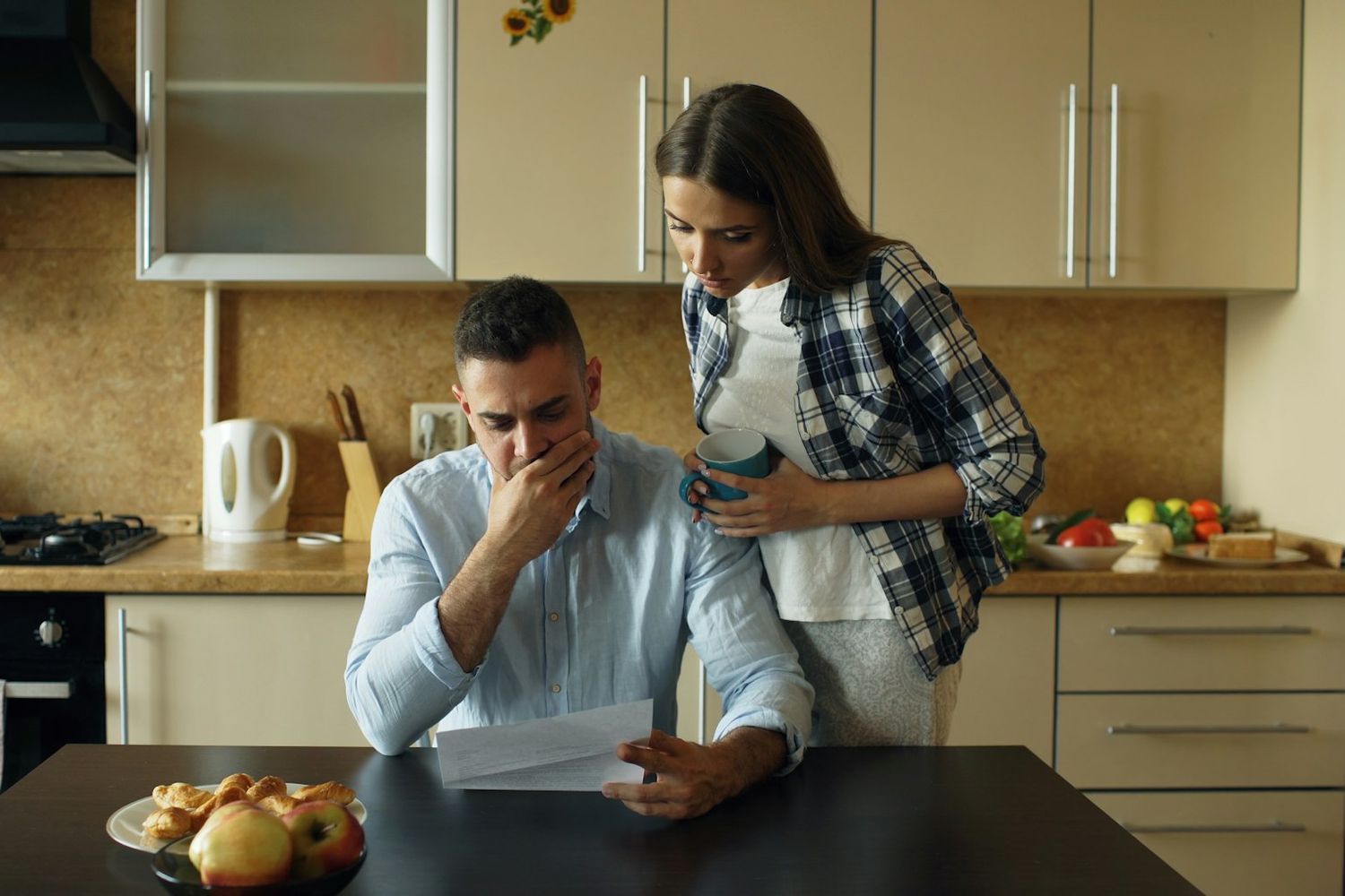 A couple in their kitchen, stressed, going through a pile of bills at the table.