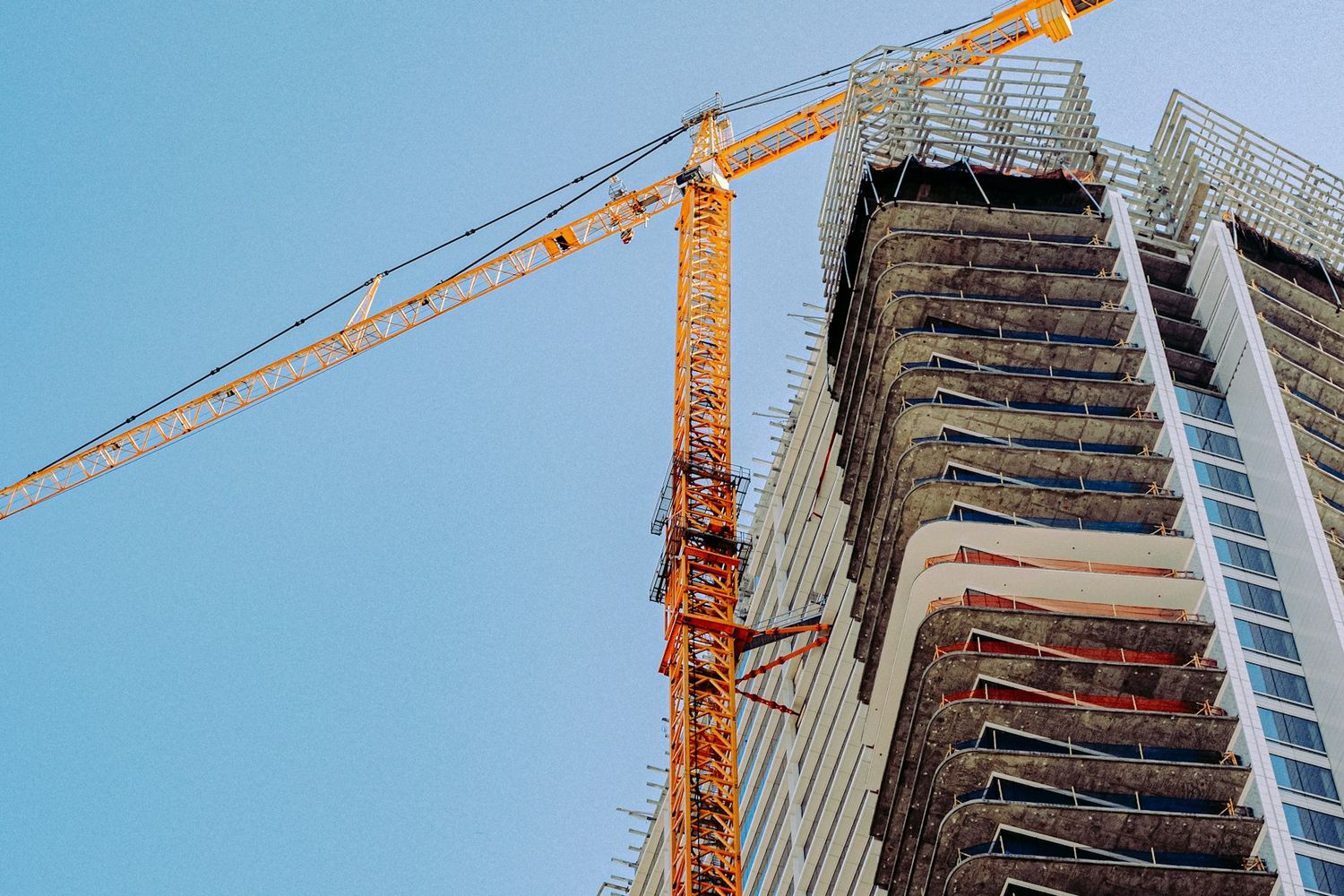 A tower crane beside a high-rise going up, against a clear blue sky.