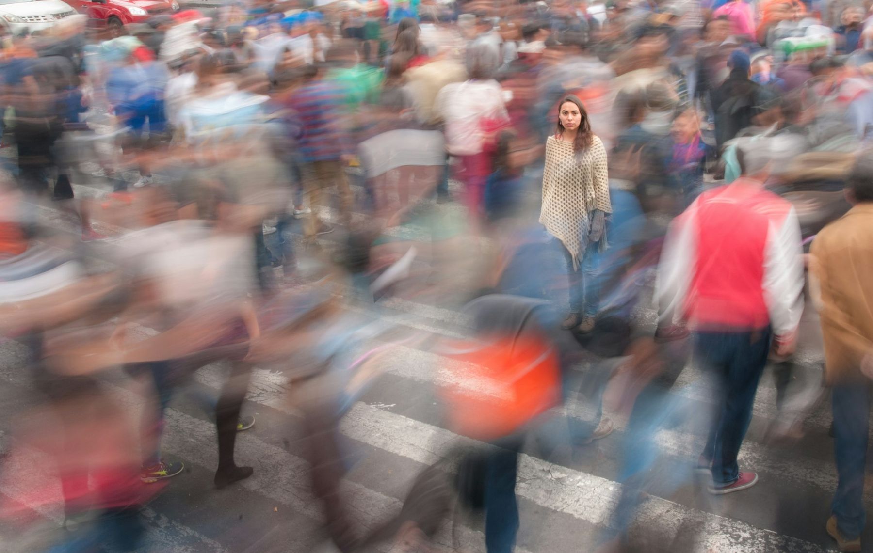 A crowd rushing across a city crossing, blurred with speed. In the middle of it, one woman stands completely still, in sharp focus.