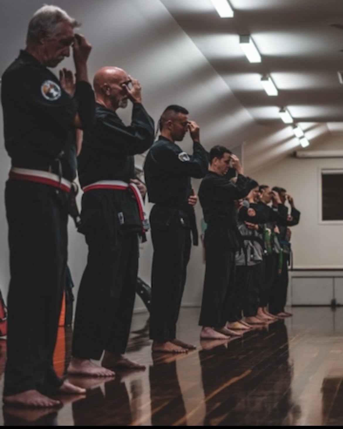 A line of martial artists in black gi standing at attention, bowing in, in a training hall.