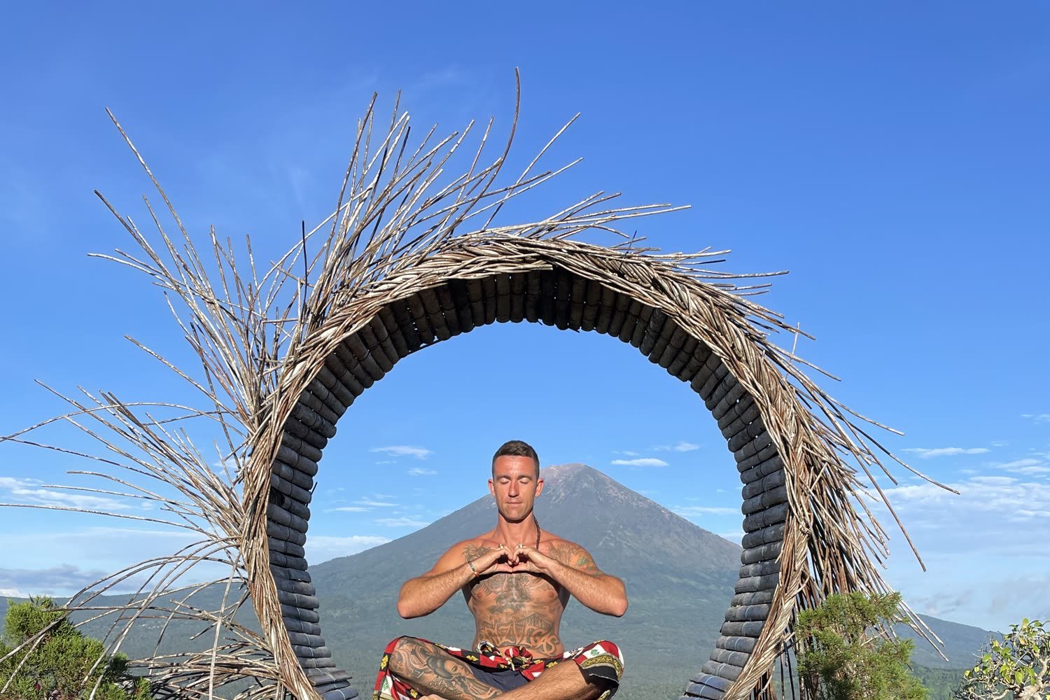 Mitch sitting cross-legged inside a woven circular frame, a mountain behind him.