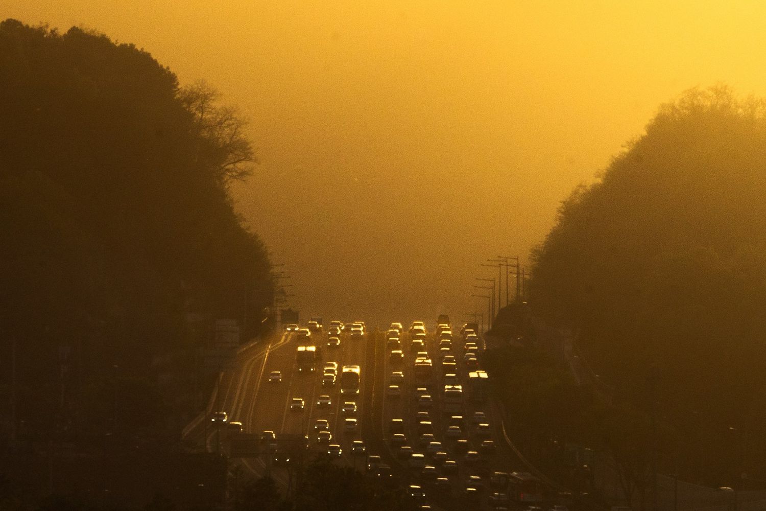 A highway jammed with traffic, headlights crawling through an orange sunset haze.
