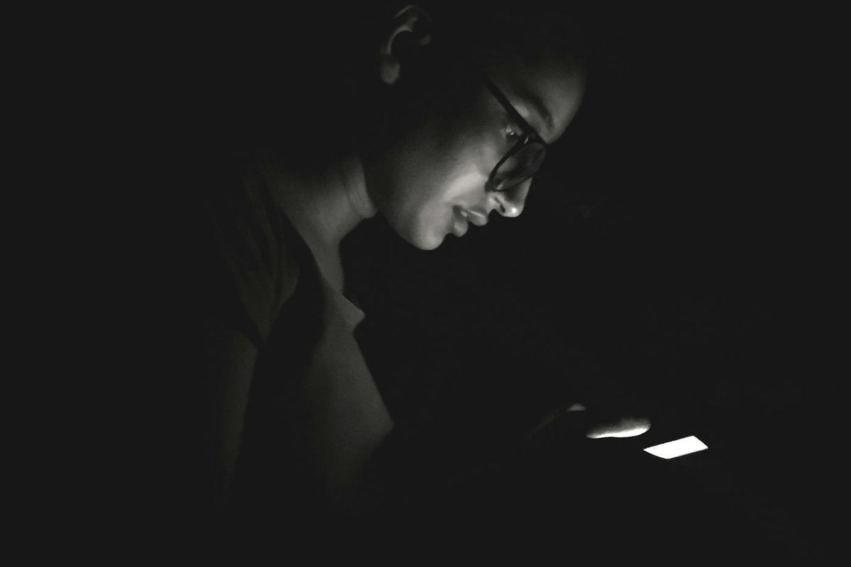 A man&rsquo;s face in a dark room, lit from below by the glow of his phone.