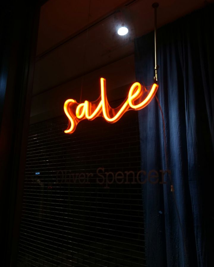 A neon sign reading &ldquo;sale&rdquo; glowing orange in a dark shop window.